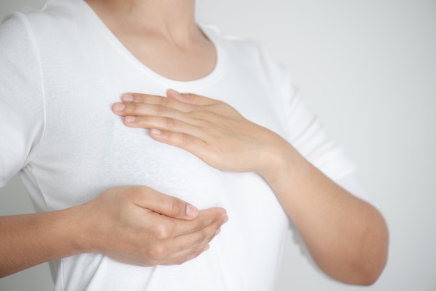 Photo woman hands checking lumps on her breast for signs of breast cancer on gray