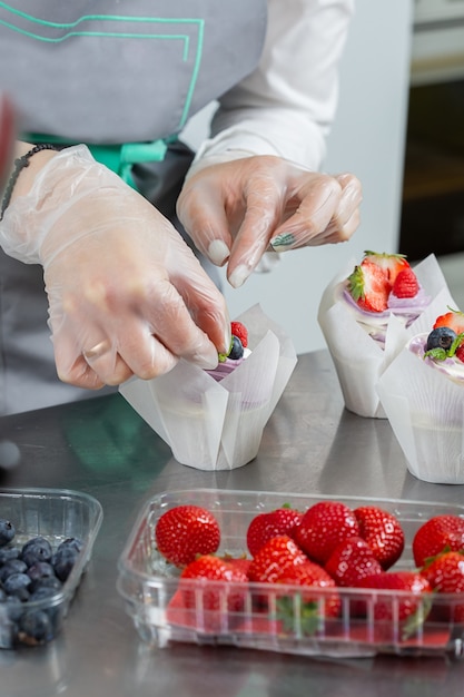 woman hands chef decorating cupcakes with pink butter cream and fresh berries