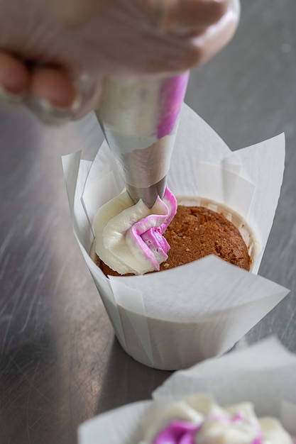  woman hands chef holding pastry bag, squeezing the cream on the cupcakes.