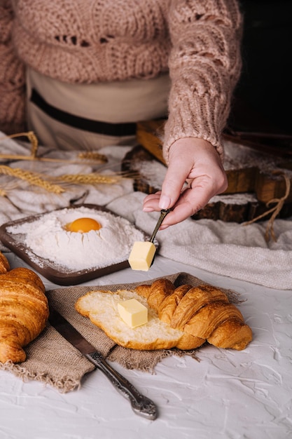 Woman hands cut a fresh croissant and spreading butter