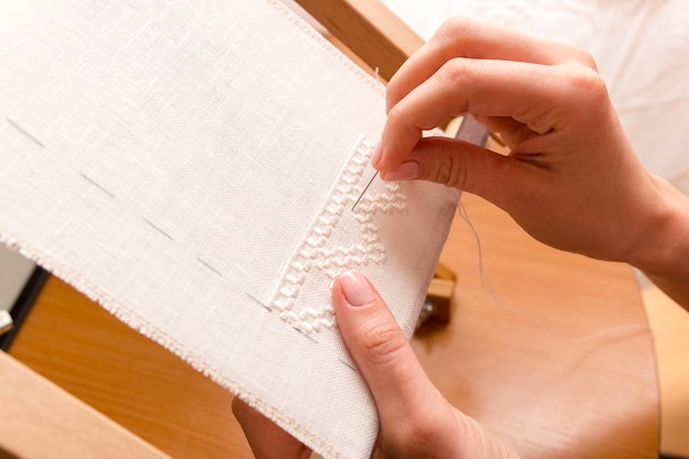 Woman hands doing cross-stitch. Close up of embroidery.