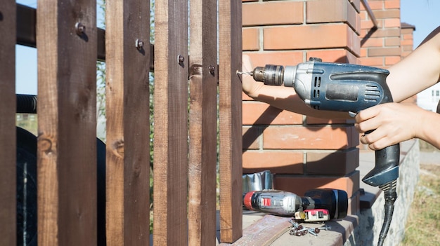 金属構造に木の板のフェンスを掘削する女性の手ドリルとネジで木製の柵を構築する