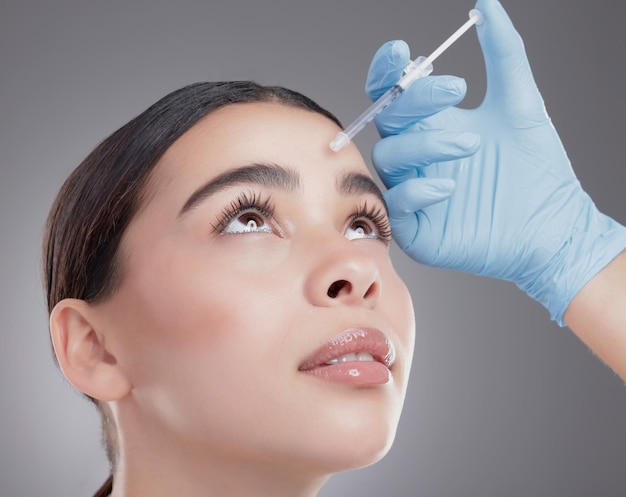 Woman hands and forehead injection in studio skincare and cosmetic service  on gray background Female person needle and plastic surgery or botox  treatment syringe and implant or beauty filler | Premium Photo