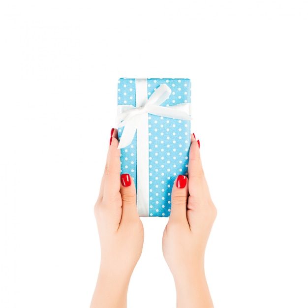 女性の手は、青い紙の白いリボンで包まれたクリスマスや他の休日の手作りプレゼントを与えます。白、トップビューで分離されました。感謝祭ギフトボックス