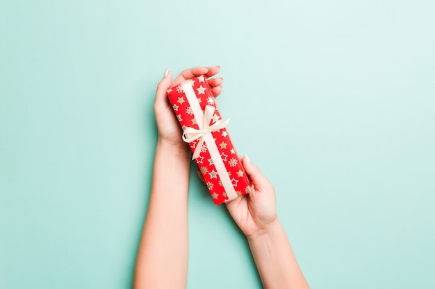 Woman hands give wrapped christmas or other holiday handmade present in colored paper 