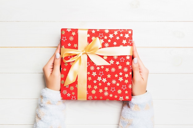 Woman hands give wrapped christmas or other holiday handmade present in colored paper