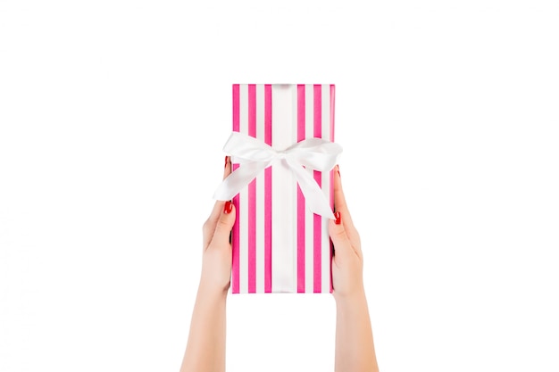 Woman hands give wrapped Christmas or other holiday handmade present in pink paper  white ribbon. Isolated on white , top view. thanksgiving Gift box 