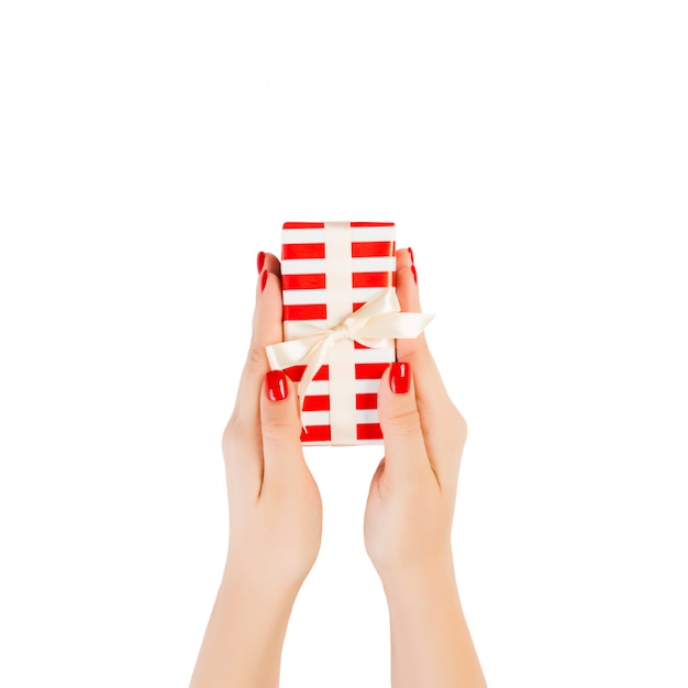 Woman hands give wrapped Christmas or other holiday handmade present in red paper with gold ribbon. Isolated on white 