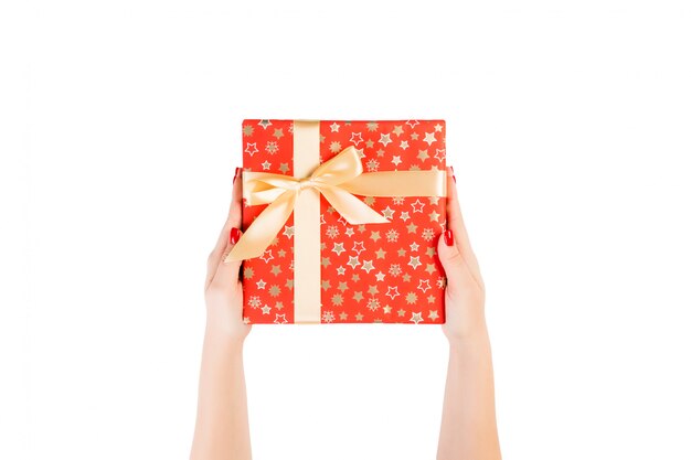 Woman hands give wrapped Christmas or other holiday handmade present in red paper with Gold ribbon