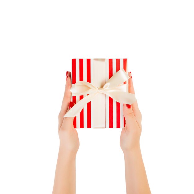 Woman hands give wrapped Christmas or other holiday handmade present in red paper with gold ribbon.