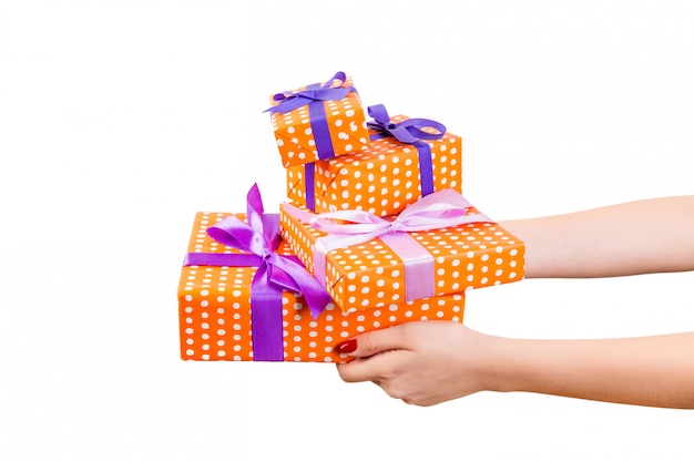 Woman hands give wrapped set of Christmas or other holiday handmade present in orange paper with purple ribbon. 