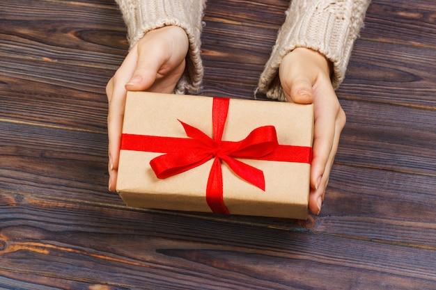 Woman hands give wrapped valentine or other holiday handmade present in paper with red ribbon.