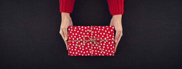 Woman hands giving christmas gift box on black background