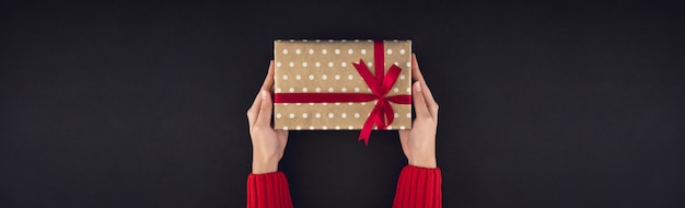 Woman hands giving christmas gift box on black background