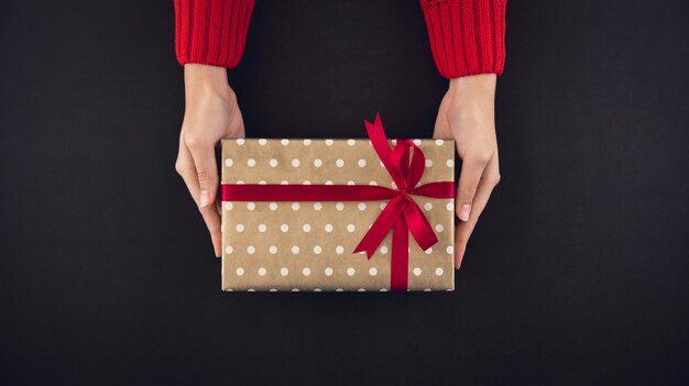 Woman hands giving christsmas gift box top view on black background