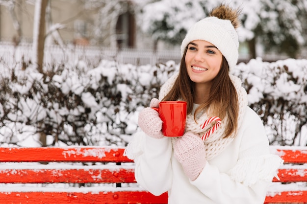 Woman hands in gloves holding a cozy mug with hot cocoa, tea or coffee and a candy cane. 