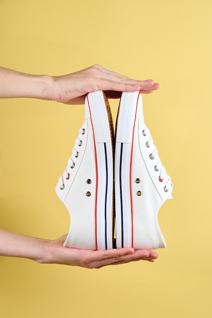 Woman hands hold casual shoes on yellow background