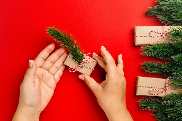 女性の手はクリスマスツリーフレームと赤い背景にモミの小枝とギフトボックスを保持します。