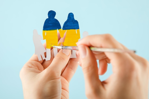 Woman hands hold a papercut family painted in the national colors of ukraine