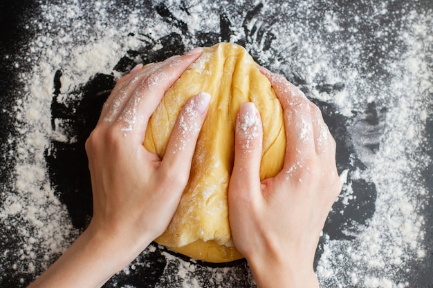 Woman hands hold prepared dough on black table