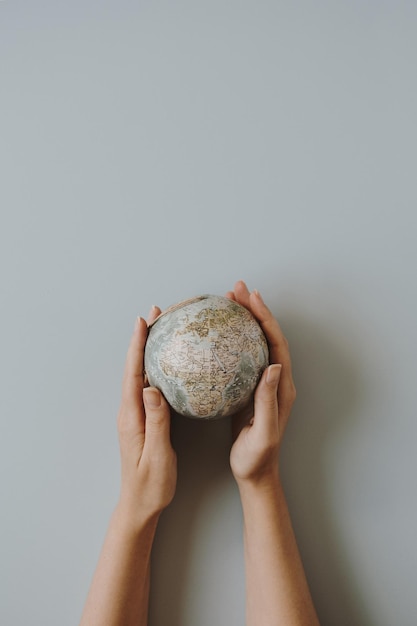 Woman hands hold small globe on blue background World planet Earth model in hands Save the Earth and environment concept Flat lay top view