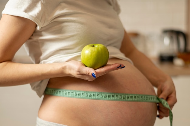 Woman hands holding an apple and measuring her belly