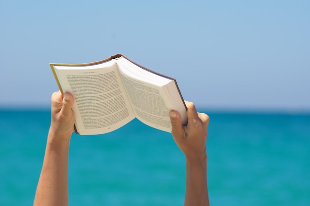 Woman hands holding book and reading on the sea