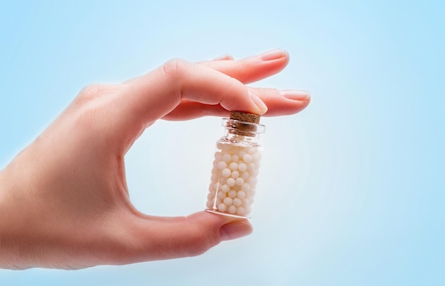 Woman hands holding a bottle with homeopathic pills on white background