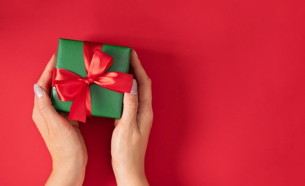 Woman hands holding Christmas present Gift box wrapped in green paper with red ribbon