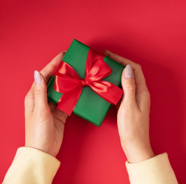 Woman hands holding Christmas present Gift box wrapped in green paper with red ribbon