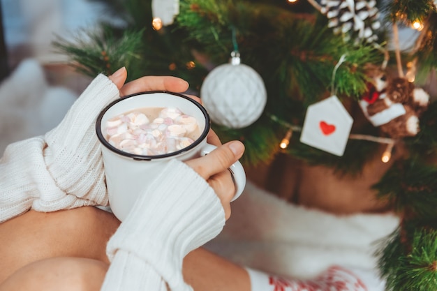 Woman hands holding coffee mug near christmas tree copy space