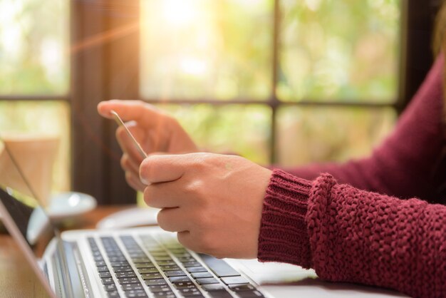 Woman hands holding a credit card and using laptop computer on table.