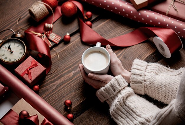 Woman hands holding cup of coffee on wooden table in wrapping time