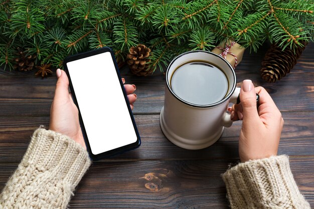 woman hands holding cup of hot coffee and phone Top view on wood