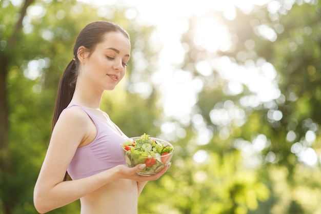 ボウルに生野菜きゅうりトマトレタスと新鮮な夏のサラダを保持している女性の手。