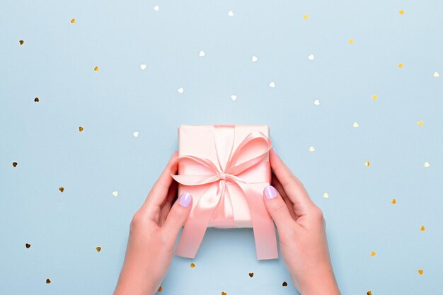 사진 파스텔 블루 배경에 분홍색 선물 상자를 들고 있는 여자 손