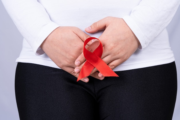 Woman hands holding her crotch with Red AIDS awareness ribbon.