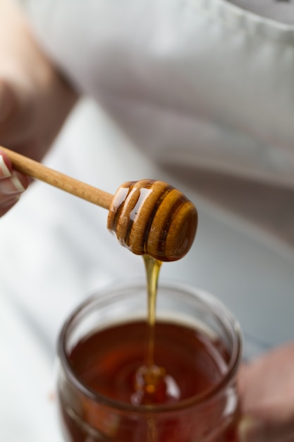 Photo woman hands holding honey spoon dipper pouring honey in jar. closeup. toning. lifestyle..