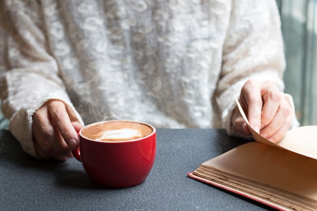 Woman of hands holding hot cup of coffee latte near window morning light.