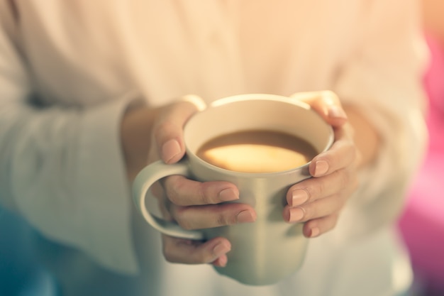 朝の日差しでコーヒーや紅茶の熱いカップを保持している女性の手。