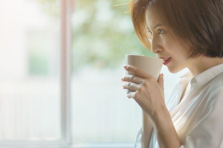 Photo 朝の日差しでコーヒーや紅茶の熱いカップを保持している女性の手。