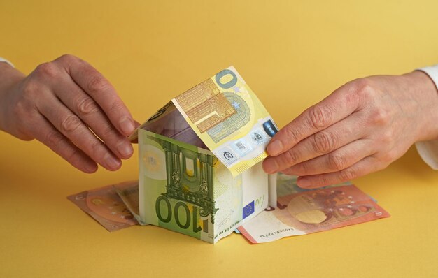 テーブルの上のユーロ紙幣で作られた家を保持している女性の手