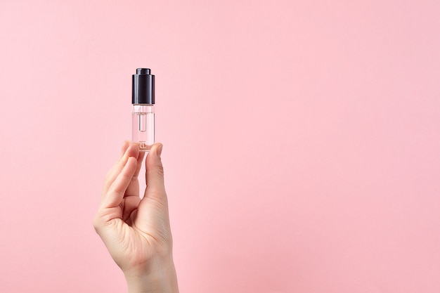 Woman hands holding hydrating facial serum, skin care product over the pink pastel background.