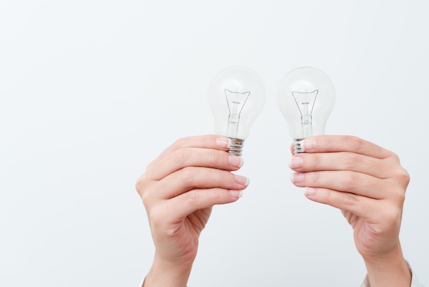 Woman Hands Holding Lamp Presenting Ideas For Project, Man Palm Showing Bulbs And New Technologies, Two Held Lightbulbs Exhibiting Another Opinion.