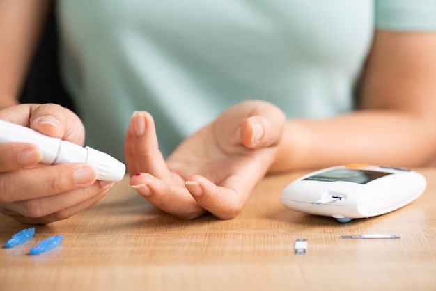 Foto la donna passa il dispositivo pungidito della tenuta con sangue per controllare il livello della glicemia