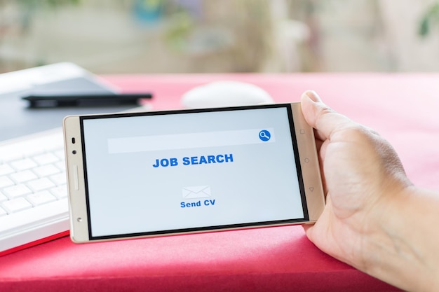 woman hands holding a mobile in which an employment website appears Work desk with keyboard