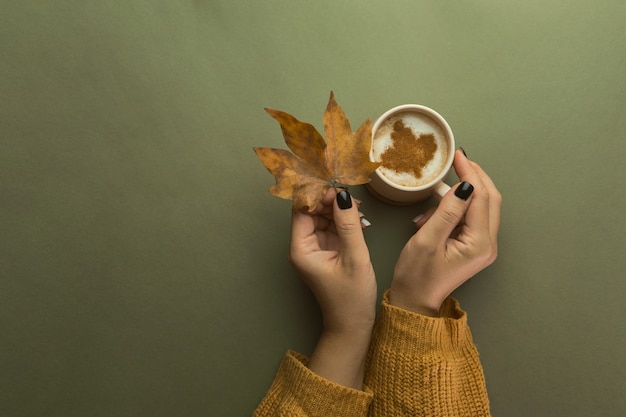 Woman hands holding morning cup of coffee decorated autumn yellow leaves