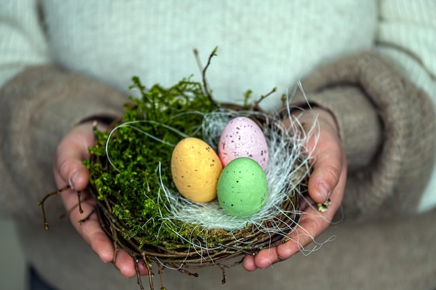 Foto mani di donna che tengono le uova di pasqua dipinte in un piccolo nido di uccelli