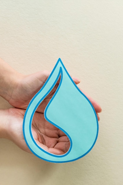 Woman hands holding paper cut water drop on beige background Clean water and sanitation saving water World Water Day Ecology concept