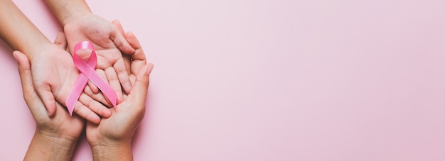 Woman hands holding pink ribbon over pink 
background, breast cancer awareness, October pink concept